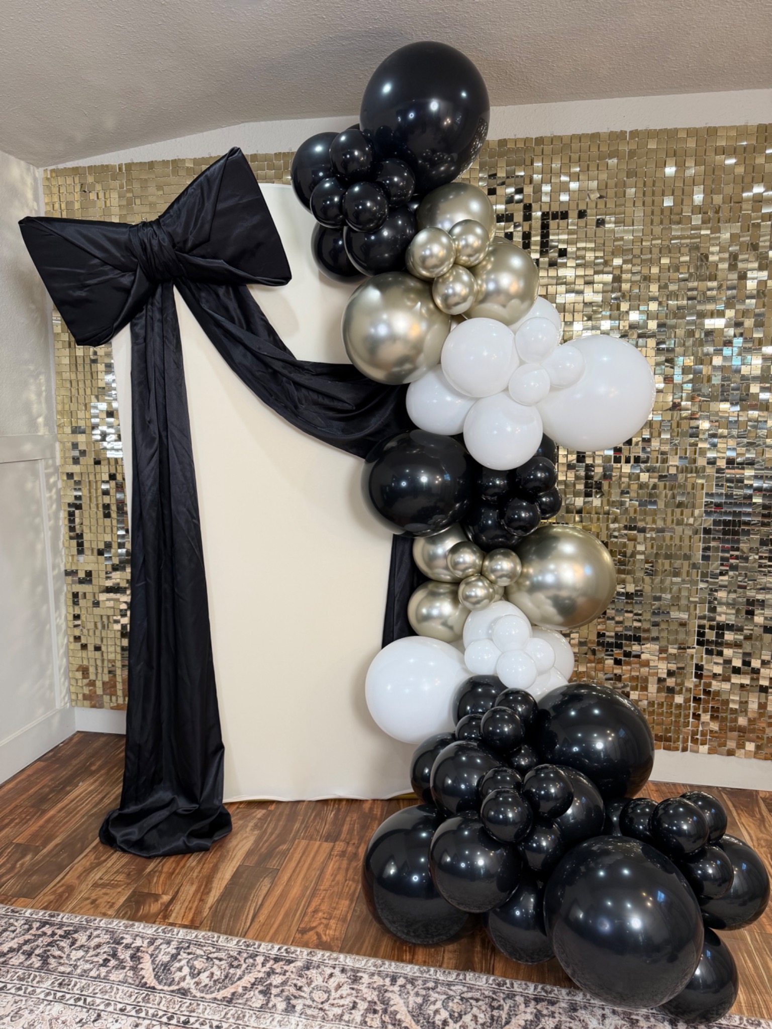Black, white and metallic balloon backdrop with a large black bow