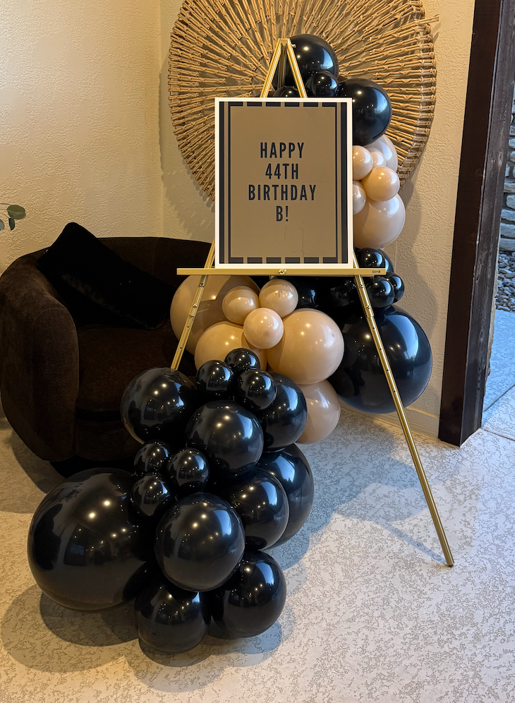 Black, gold and neutral balloons surrounding a birthday welcome sign